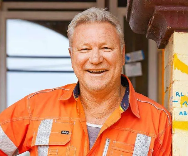 Person in orange work attire smiling in front of a building.