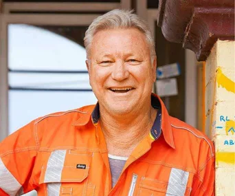 Person in orange work attire smiling in front of a building.