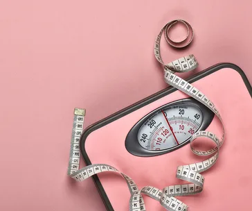 A pink bathroom scale with a coiled measuring tape on a pink background.