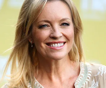 A woman with blonde hair smiling, wearing a light-colored top with a detailed pattern.