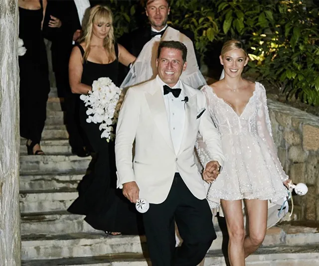 A couple in formal attire walking down stairs, smiling, with bridesmaids and groomsmen following.