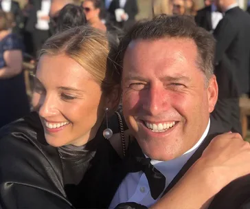 A couple smiling and embracing at an outdoor formal event.