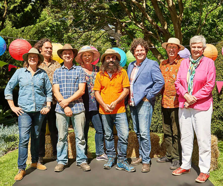 Group of eight people outdoors, wearing casual and colorful clothing, standing in front of trees and decorative lanterns.