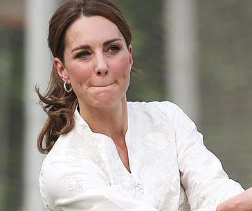 Kate Middleton in a white embroidered blouse, focused during a tennis match.