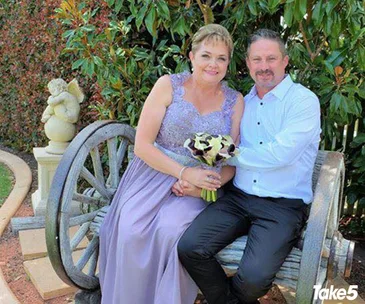 Couple sitting on a wagon wheel bench in a garden, woman holding a bouquet.