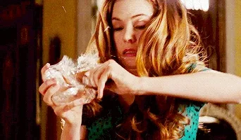 A woman with long hair frantically unwrapping an object, looking surprised and intense, inside a warmly lit room.