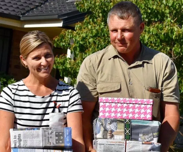 A smiling couple stands outdoors holding wrapped gifts against a sunny backdrop.