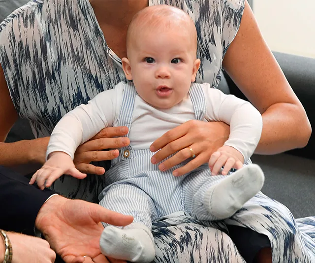 Child sitting on an adult's lap, dressed in a white top and striped overalls, with attentive expression.