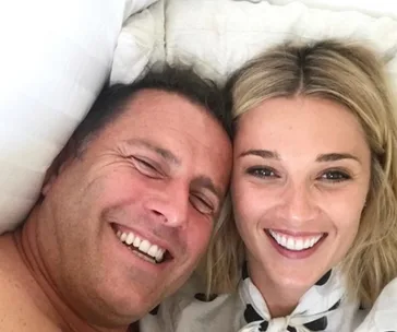 A smiling couple lying down, looking at the camera, with bright expressions.