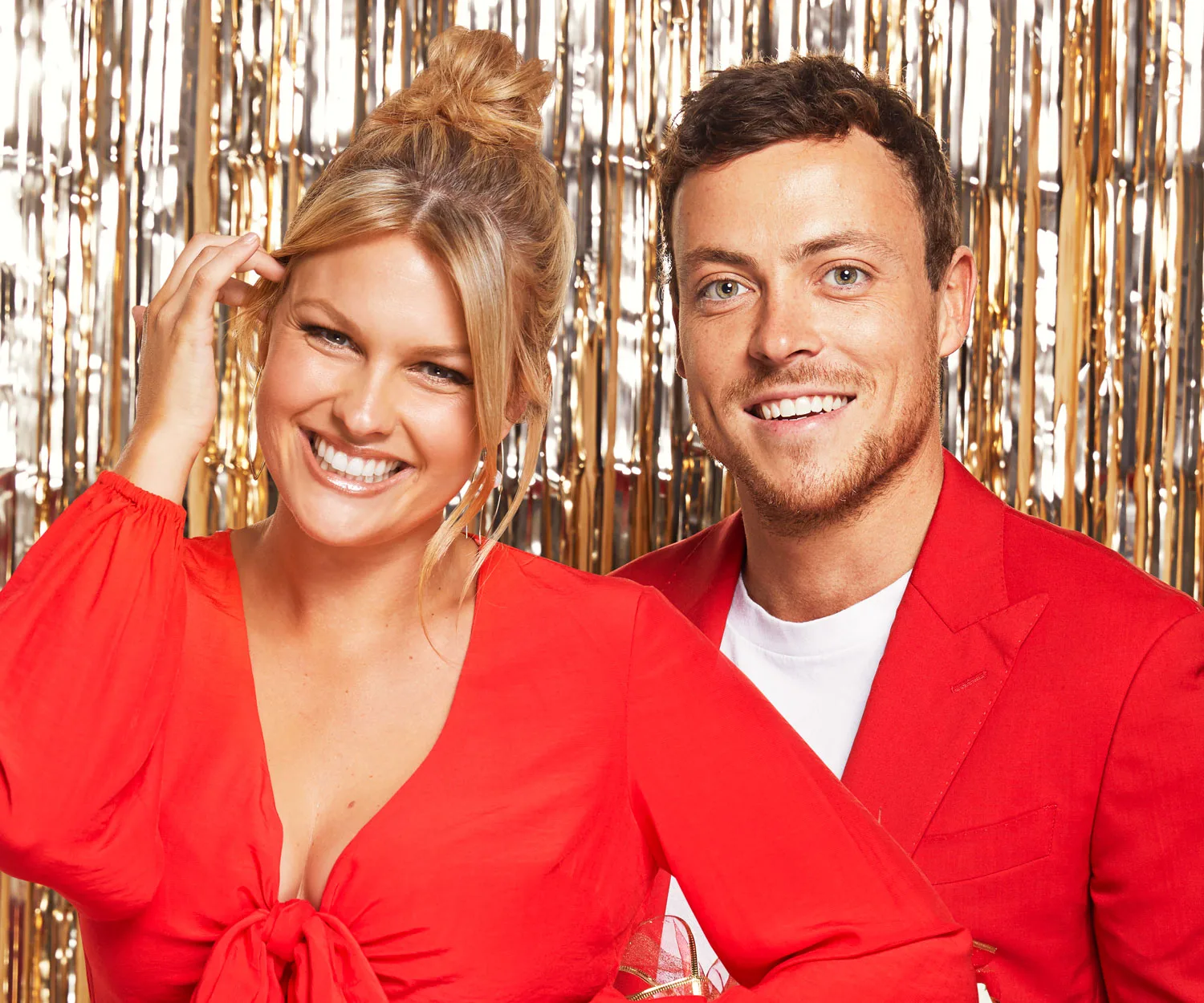 A smiling couple in red outfits against a gold tinsel backdrop.