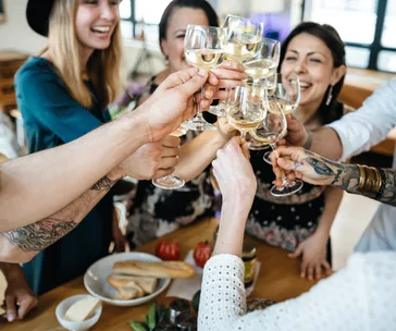 Group of friends toasting with wine glasses around a table with food, smiling and celebrating together.