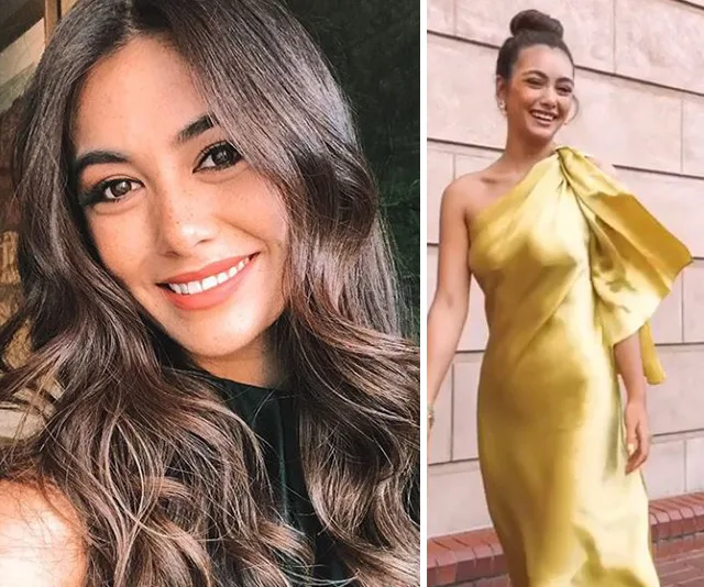 "Smiling woman with long hair; dressed in an elegant one-shoulder gold gown, posing outdoors."