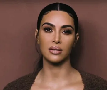 Woman with sleek dark hair and glossy lips, wearing a dark top against a neutral background.