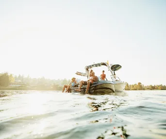Family enjoying a sunny day on a boat, relaxing by the water with trees in the background.