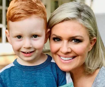 A woman with blonde hair smiles alongside a young boy with red hair, both looking at the camera.