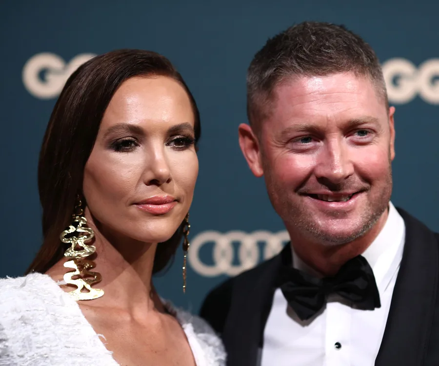 Two people posing together at a formal event with a dark green background and circular patterns.