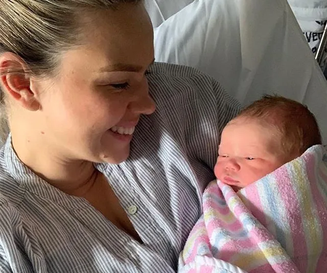 A woman smiling at a newborn baby wrapped in a striped blanket.