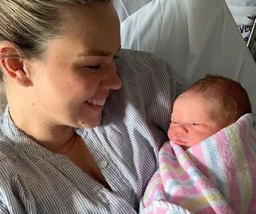 A woman smiling at a newborn baby wrapped in a striped blanket.