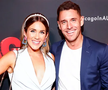 Two people smiling at an event; woman in a white top with colorful earrings and headband, man in a navy blazer.