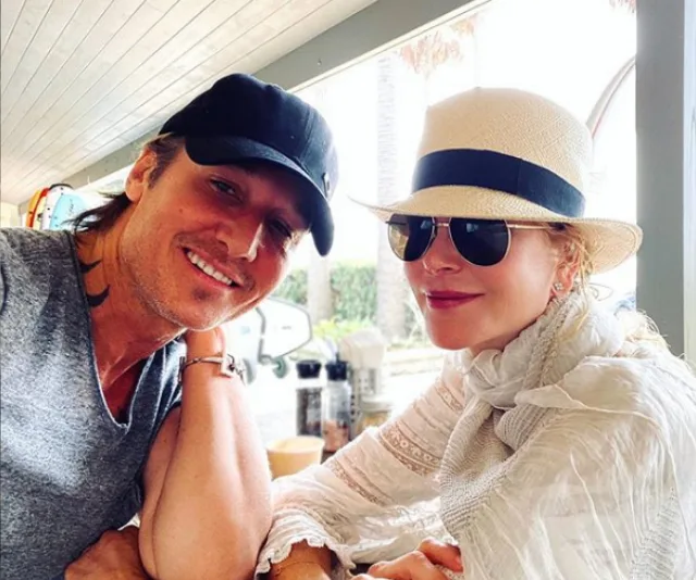 A couple smiling at a cafe, with one wearing a black cap and the other in a white hat and sunglasses.