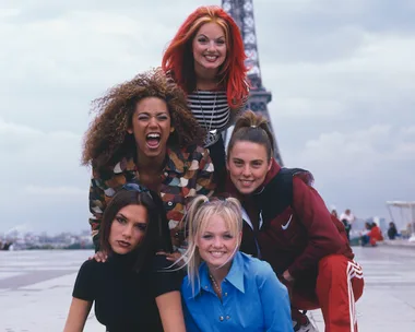 Five women posing and smiling near the Eiffel Tower with a cloudy sky in the background.