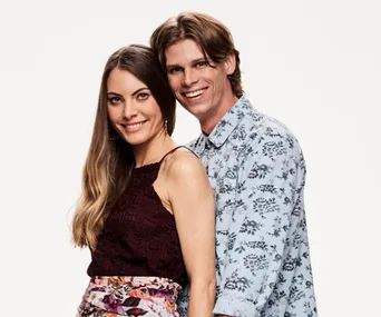 Couple posing together, the woman in a burgundy top and the man in a floral shirt, smiling against a white background.