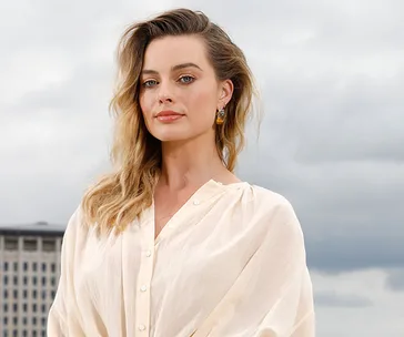 Alt text: Woman in a white blouse poses outdoors against a cloudy sky backdrop.