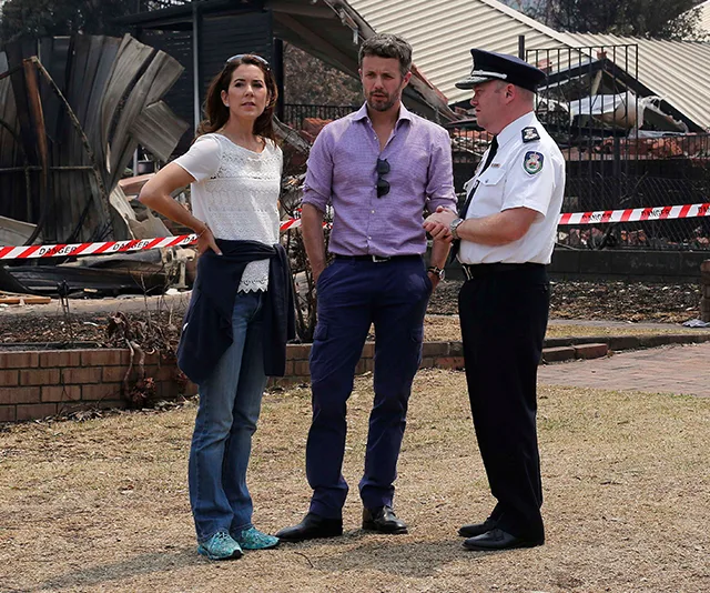 A woman and man talking to a uniformed officer in front of a fire-damaged structure with caution tape around.