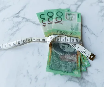 Australian currency wrapped in a measuring tape on a marble surface, symbolizing budgeting or financial planning.