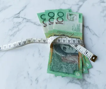 Australian currency wrapped in a measuring tape on a marble surface, symbolizing budgeting or financial planning.