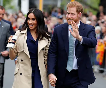 Prince Harry and Meghan Markle smiling and waving while holding hands during a public appearance in Canada, 2020.