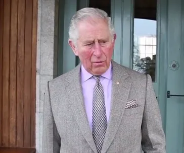 I don't know who this is, but it's a man in a suit standing outside a building with wooden and glass doors.