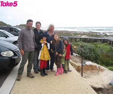 Family posing by the coast with ocean and rugged landscape in the background, labeled "Take 5" in the corner.
