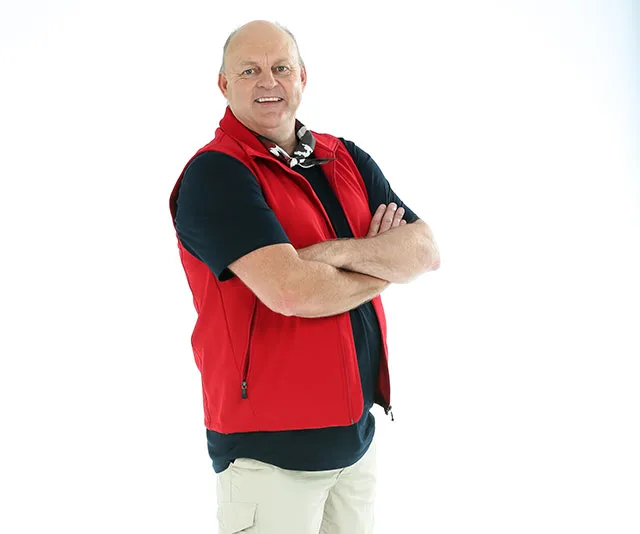 A person in a red vest and black shirt stands confidently with arms crossed, smiling against a white background.