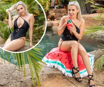 Blonde woman in black swimsuit by a pool, sipping a red drink and sitting on a watermelon-patterned towel.