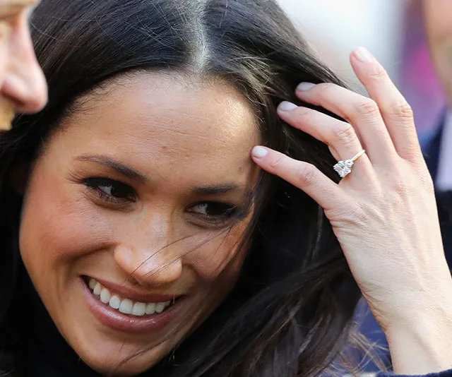 Smiling woman with dark hair shows engagement ring on left hand.