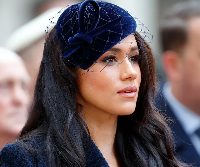 A woman with long hair wearing a navy hat with netting, looking to the side.