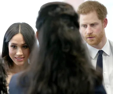 Two people engaging in conversation with another person, indoors, wearing formal attire.