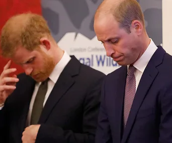 Two men in suits appear thoughtful at an event, with a wildlife conservation banner in the background.
