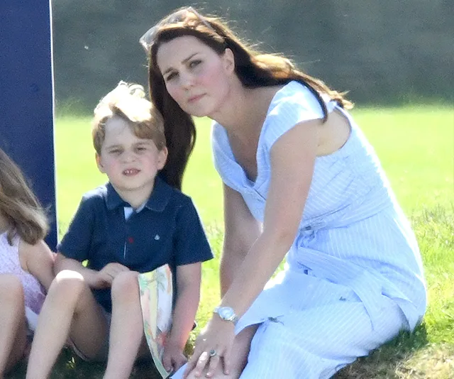 A woman in a striped dress and a young boy are sitting on the grass on a sunny day.