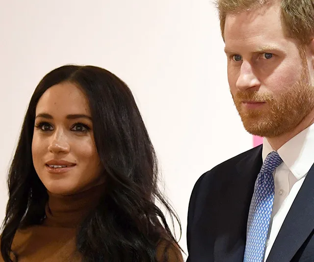 Two individuals stand together, one wearing a brown top and the other in a suit with a blue tie.