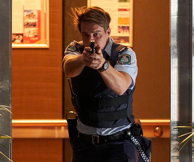 Police officer aims gun intently in a tense scene, wearing uniform in a building setting.