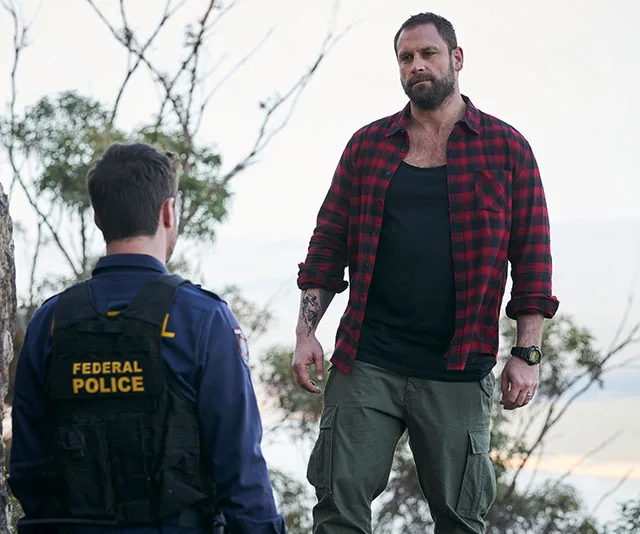 A tense scene with a rugged man in a plaid shirt facing a federal police officer in an outdoor setting.