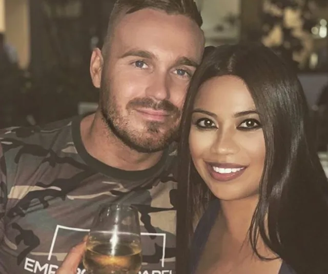 A smiling couple poses closely, with the man holding a wine glass.