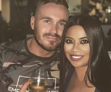 A smiling couple poses closely, with the man holding a wine glass.