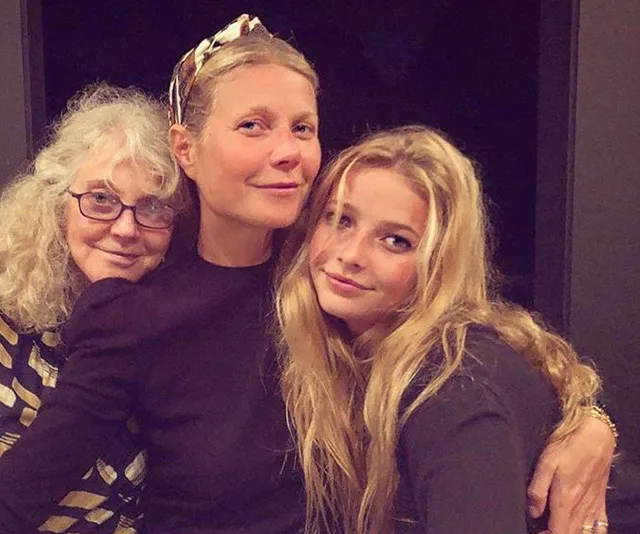 Three women standing close together, smiling, in a warm, familial embrace.