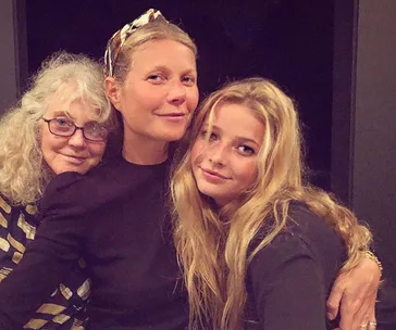 Three women standing close together, smiling, in a warm, familial embrace.
