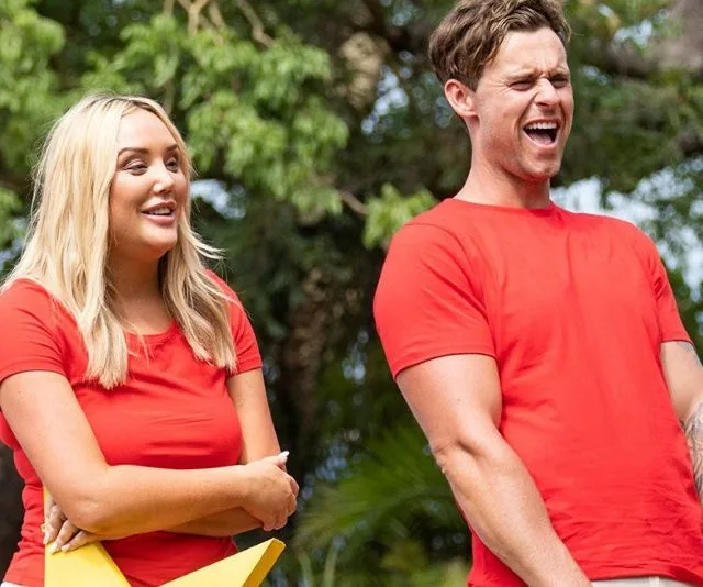 Two people wearing red shirts laughing outdoors, surrounded by greenery.