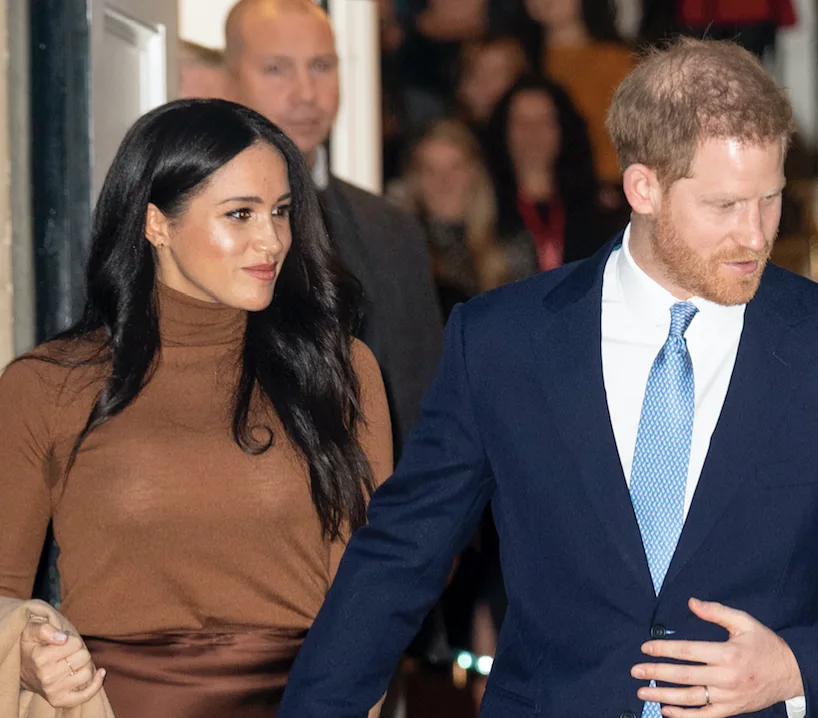 Couple walking together in a crowded setting, the woman in a brown outfit and the man in a blue suit.