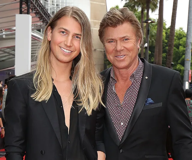 Two people in formal attire smiling at a red carpet event.